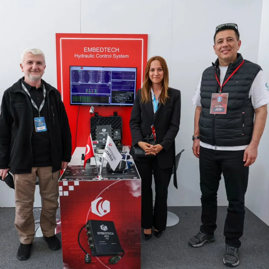 EFES 2026’daki EmbedTech standı: masada EmbedTech HCS, arkada test arayüzü ekranı ve standın önünde üç kişi